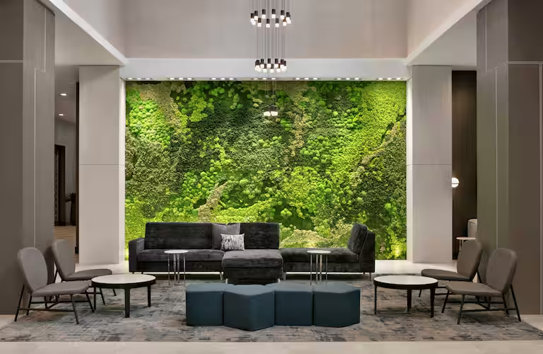 Modern lounge area featuring a green moss wall, comfortable gray seating, and contemporary round tables.